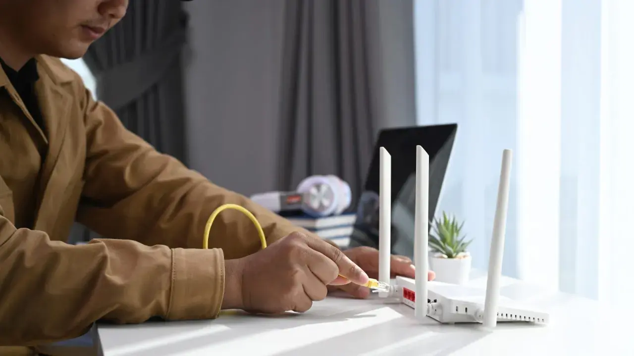 Mann schließt ein Netzwerkkabel an einen Router an, um seinen Laptop als Router zu verwenden.