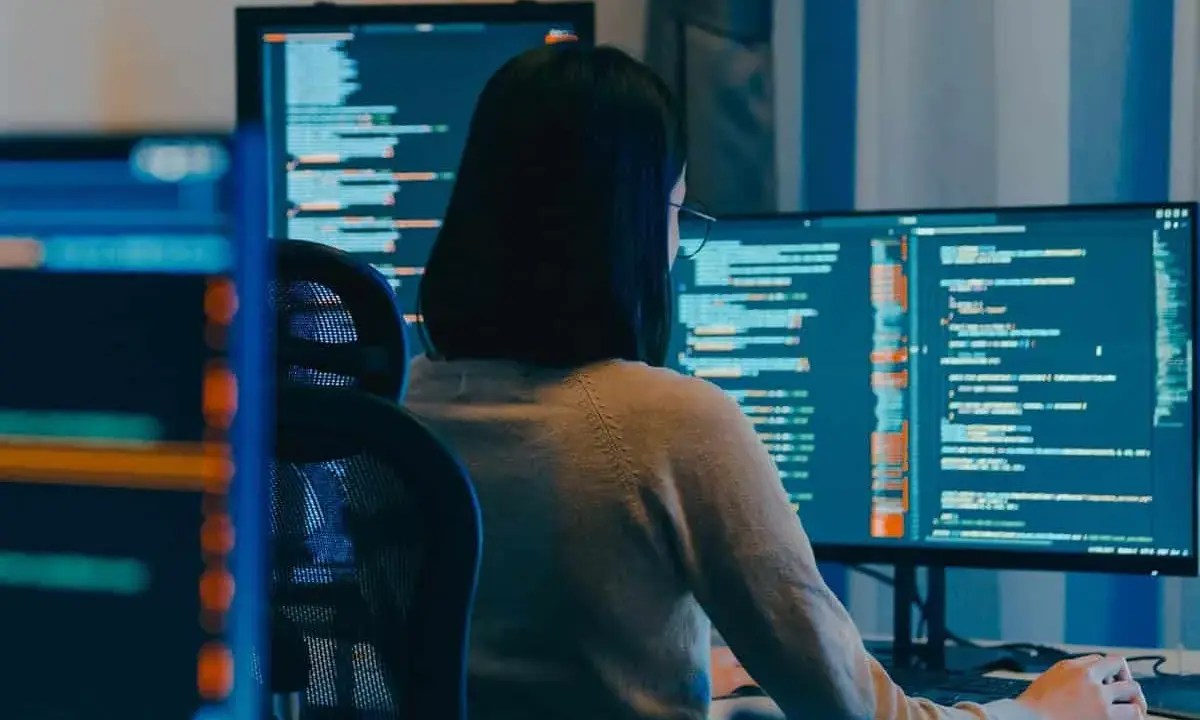 Eine Person mit Brille arbeitet an mehreren Bildschirmen, die Code anzeigen. Die **windows vollbild** Ansicht auf dem Hauptmonitor ist klar erkennbar.