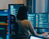 Eine Person mit Brille arbeitet an mehreren Bildschirmen, die Code anzeigen. Die **windows vollbild** Ansicht auf dem Hauptmonitor ist klar erkennbar.