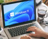 Mann tippt auf Laptop mit Windows 11. Ein netspeedmonitor könnte hier nützlich sein, um die Leistung zu prüfen.