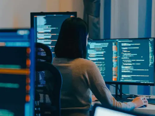 Eine Person mit Brille arbeitet an mehreren Bildschirmen, die Code anzeigen. Die **windows vollbild** Ansicht auf dem Hauptmonitor ist klar erkennbar.