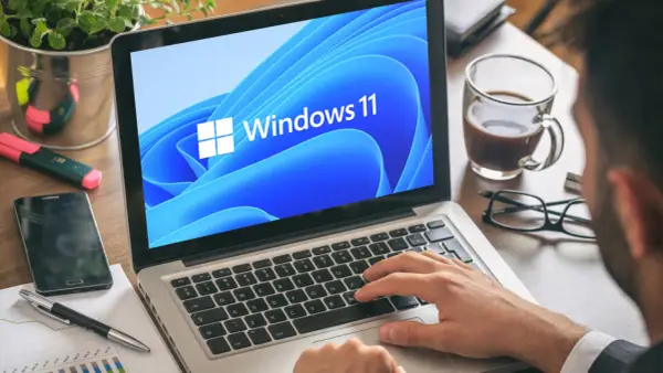 Mann tippt auf Laptop mit Windows 11. Ein netspeedmonitor könnte hier nützlich sein, um die Leistung zu prüfen.